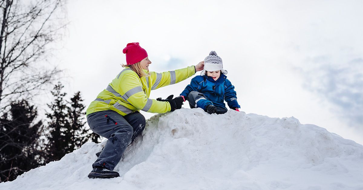 Förskolepedagog hjälper litet barn uppe på en snöhög.