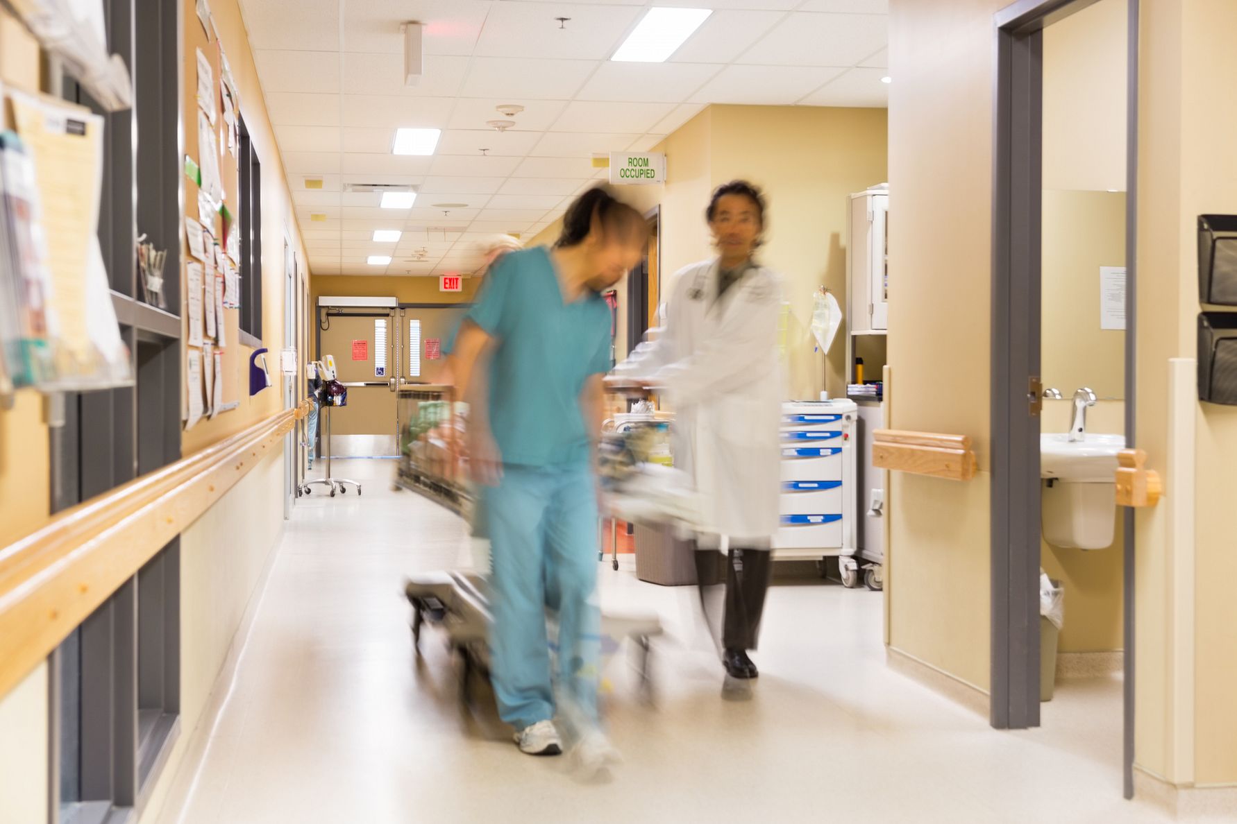 Vårdpersonal drar en säng i sjukhuskorridor