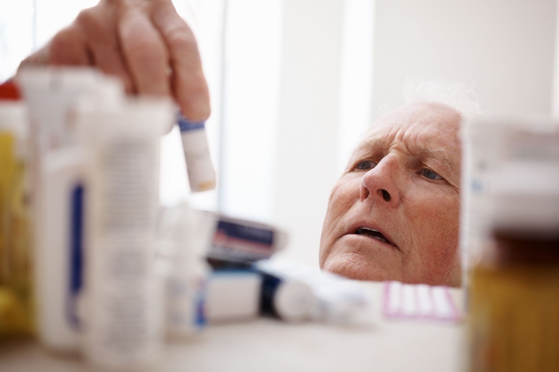 Äldre man tar medicinflaska från en hylla