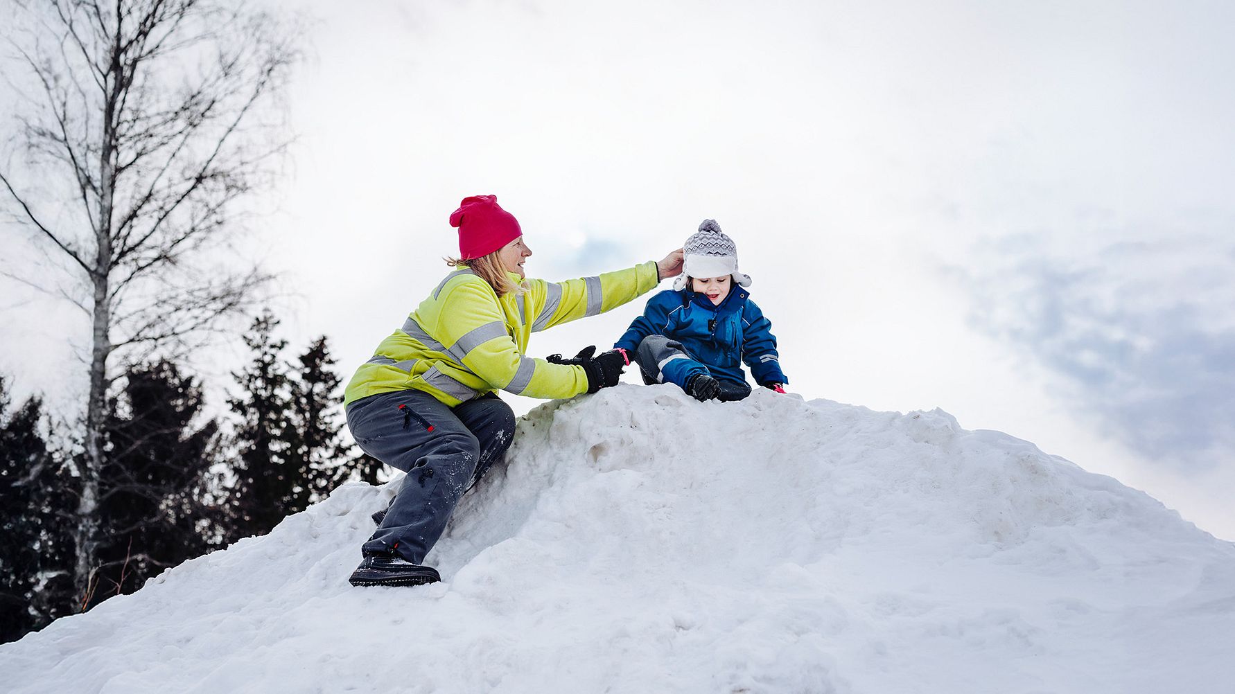 Förskolepedagog hjälper litet barn uppe på en snöhög.