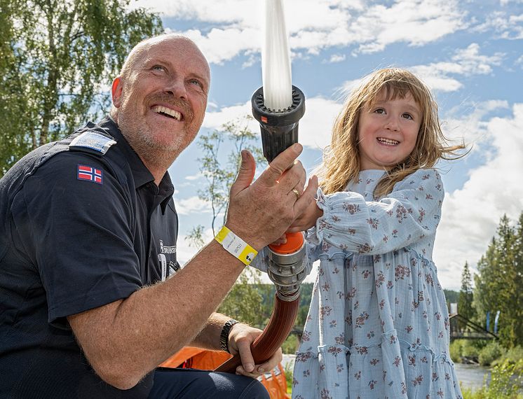 En brannmann som hjelper en liten jente å spyle med brannslange.