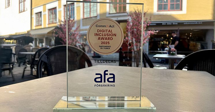 Priset i tävlingen CommToAct – Digital Inclusion Award 2025 står på ett ljusgrått bord med en äldre fasad i gult i bakgrunden