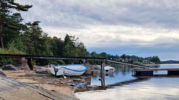 Bilden visar en liten båt som ligger förtöjd vid en brygga i en sjö. Vattennivån i sjön är så låg att båten ligger på land.