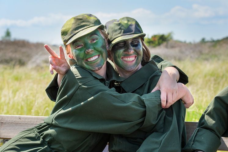 Två unga tjejer i grön overall och militärkeps kramas.