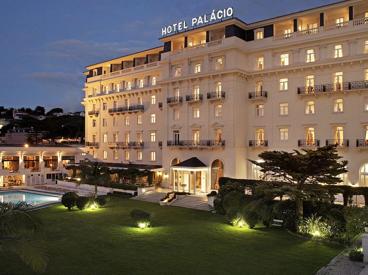 Hotel Palácio Estoril valaistuna iltahämärässä. Rakennus loistaa uljaana pimeässä ja viestii ylellisyyttä.