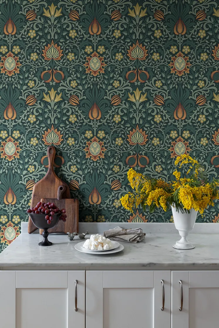Kök med detaljrik botanisk tapet i mörkgröna, orange och gula toner, marmorbänk och vas med gula blommor.