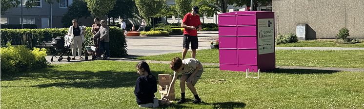 Barn leker i gräset med ett super-jenga spel framför en rosa Pifflbox från Leksaksbiblioteket. 