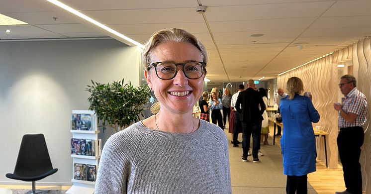 Lydia Kwak har en stickad grå tröja på sig, brunbågade glasögon, blont uppsatt hår och ler.
