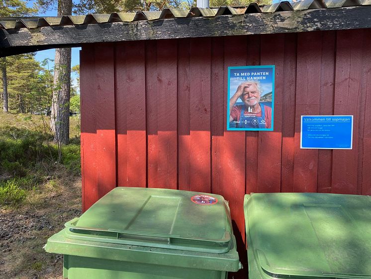 Affisch på en röd husfasad, två gröna sopkärl med stickers