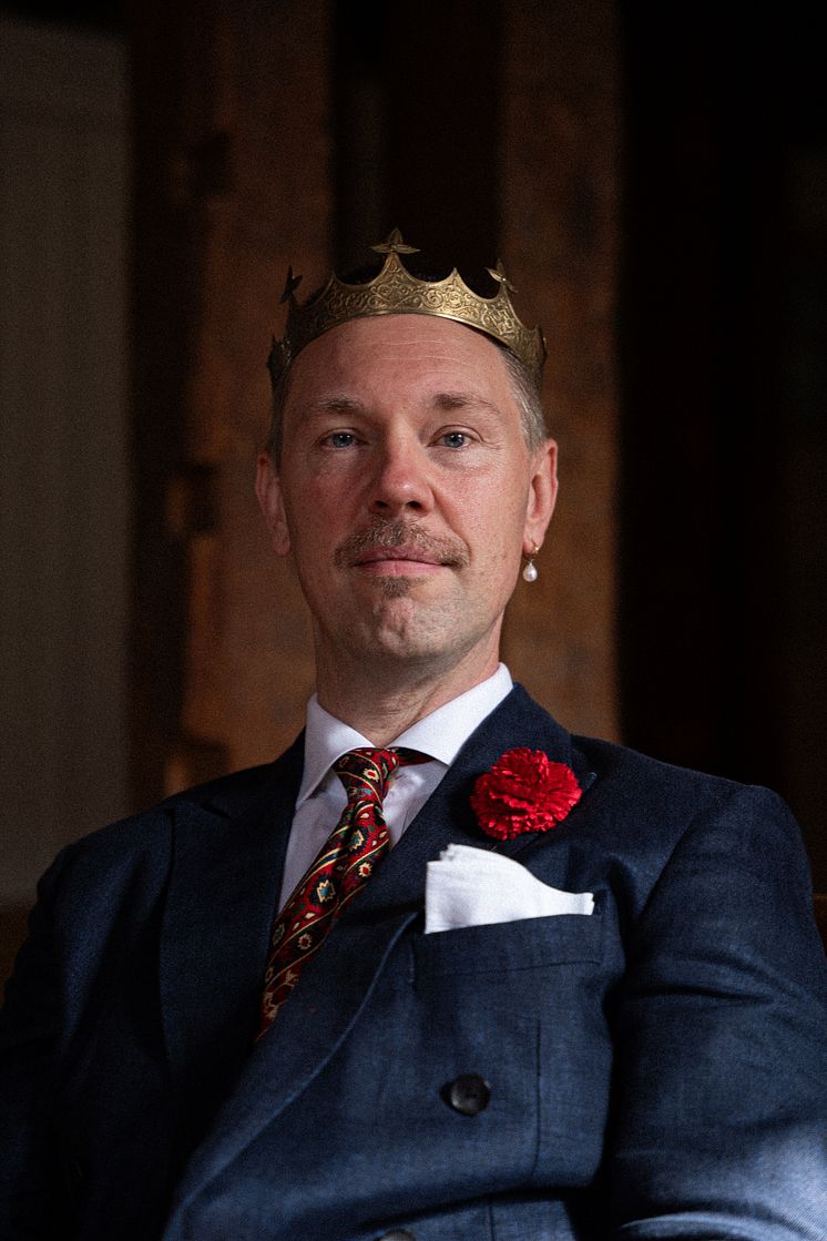 Porträtt av man med guldkrona och röd nejlika i kavajslaget.