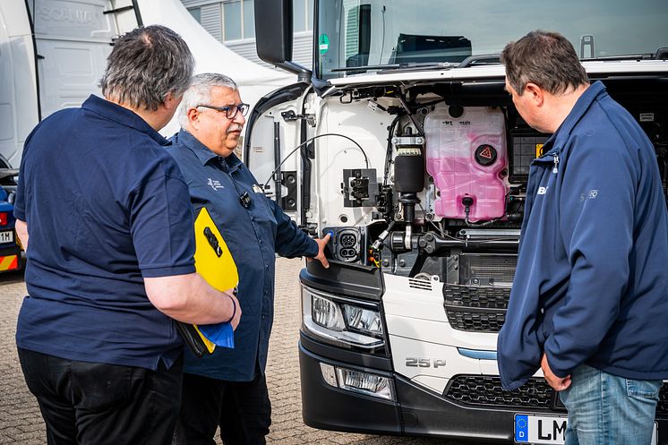 Fahrlehrer Frank Hartmann erklärt den Bona-Werksfahrern Enrico Wachsmann und Gunther Heinritz, wo und wie der vollelektrische Scania 25 P geladen wird.