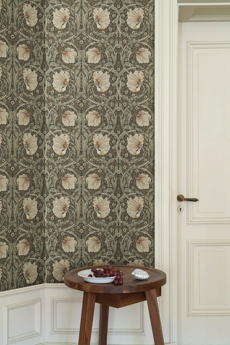Detaljrik tapet med stiliserade blommor och blad i dämpade gröna och beige toner, intill en vit spegeldörr och ett träbord.