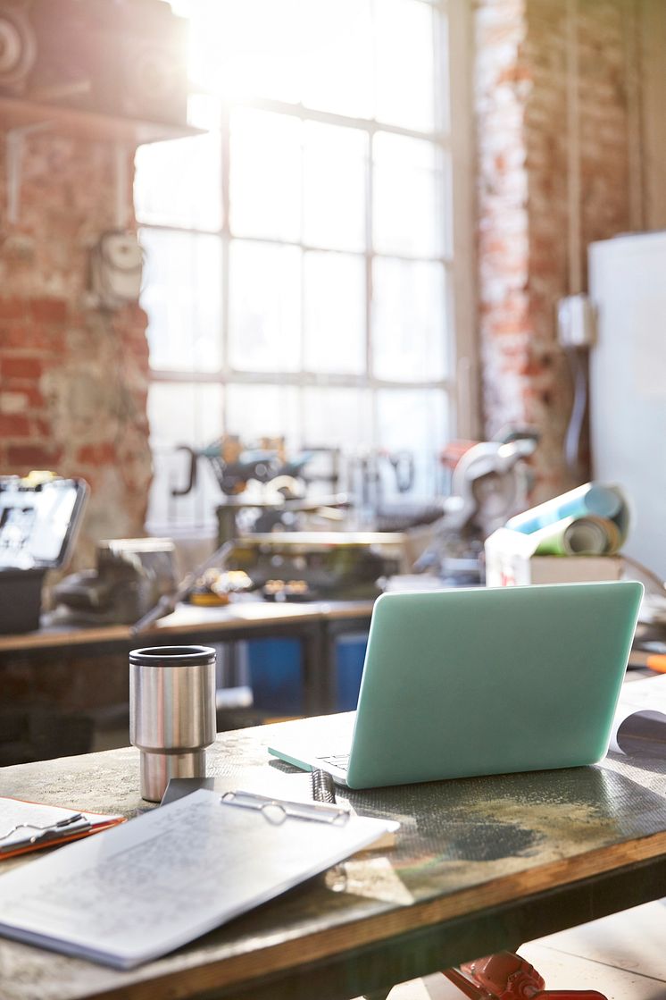 Laptop, coffee and clipboard on workbench in workshop_Agnieskza Olek_GettyImages-750415345