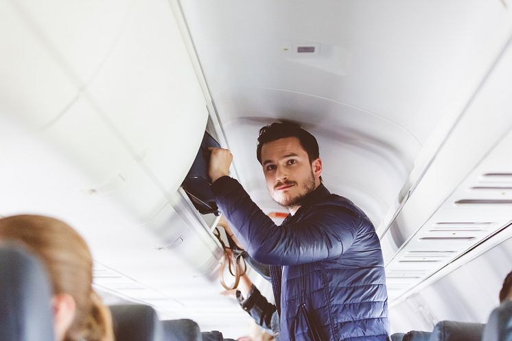 THEME_TRAVEL_AIRPORT_AIRPLANE_PEOPLE_MALE_PASSENGER_STORING_HAND_LUGGAGE_IN_THE_OVERHEAD_LOCKER_GettyImages-846448616_Universal_Within usage period_99793