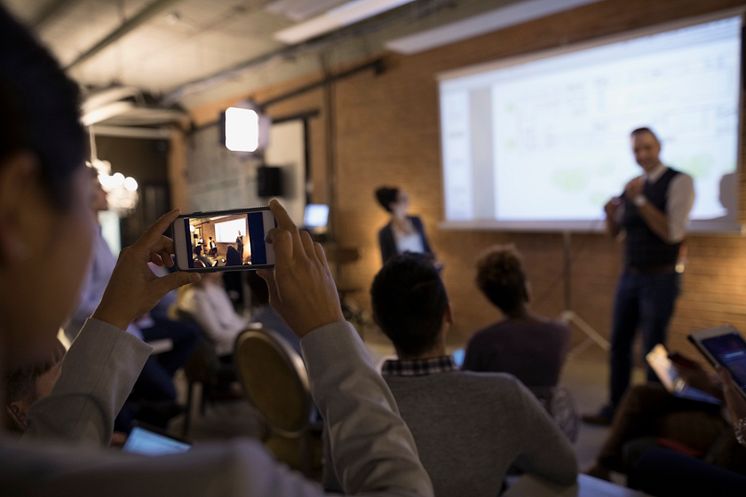 Businesswoman with camera phone videoing conference speaker in conference room