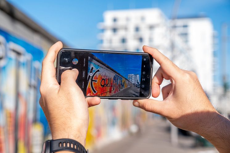 Berlin_Person_macht_ein_Handyfoto_von_Berliner_Mauer_mit_Eastside_Gallery