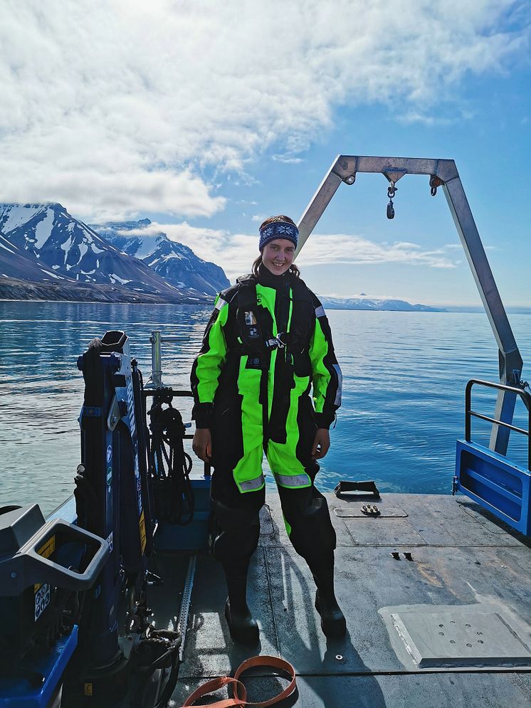 Forskare i grön och svart klädsel står på båtdäck i Svalbard.