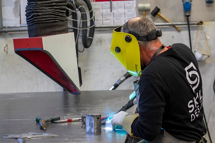 Beholder en fot i det tradisjonelle. Punktsveising utføres daglig, når metallskilt og rammer skal monteres sammen.