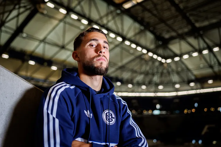 Adil Aouchiche steht in der VELTINS-Arena und blickt ernst in die Kamera.