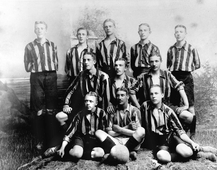Ett fotbollslag bestående av allvarliga unga män i randiga tröjor. Ateljébild från sekelskiftet 1900-talet. Foto: Hedvig Rosendahl, Nordiska museet.