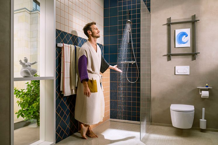 Ein Mann steht mit einem Bademantel in der Dusche und halt seine Hand in den Wasserstrahl einer Handbrause von Hansgrohe