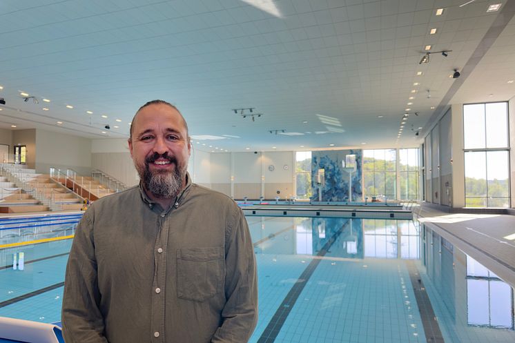 Kommunantikvarie Dan Cardesjö står framför 50 metersbassängen med hopptornsväggen längst in.jpg