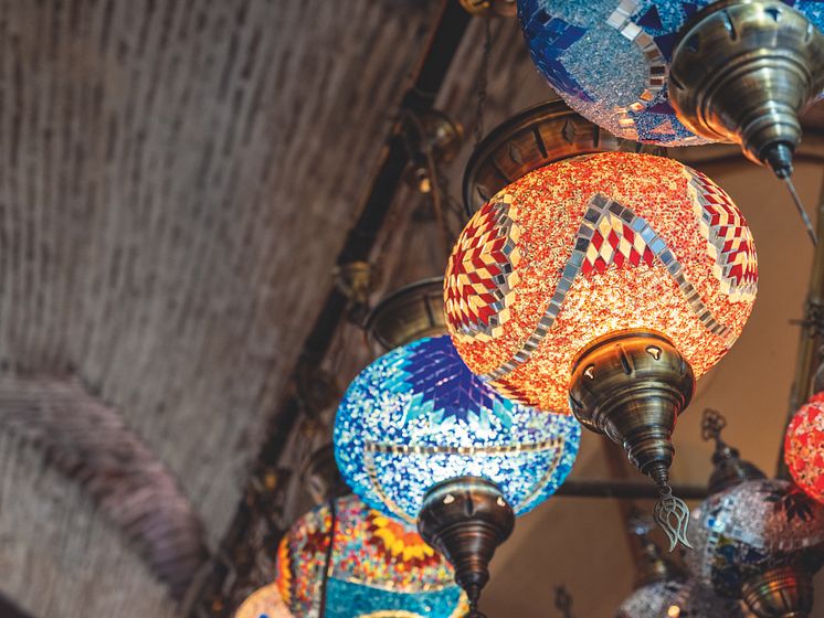 Kuva värikkäistä mosaiikkilampuista, jotka roikkuvat tiiliholvikatosta. Lampuissa on monivärisiä, koristeellisia kuvioita