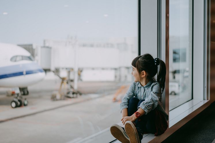 Preschool girl sitting by window at airport and looking outside