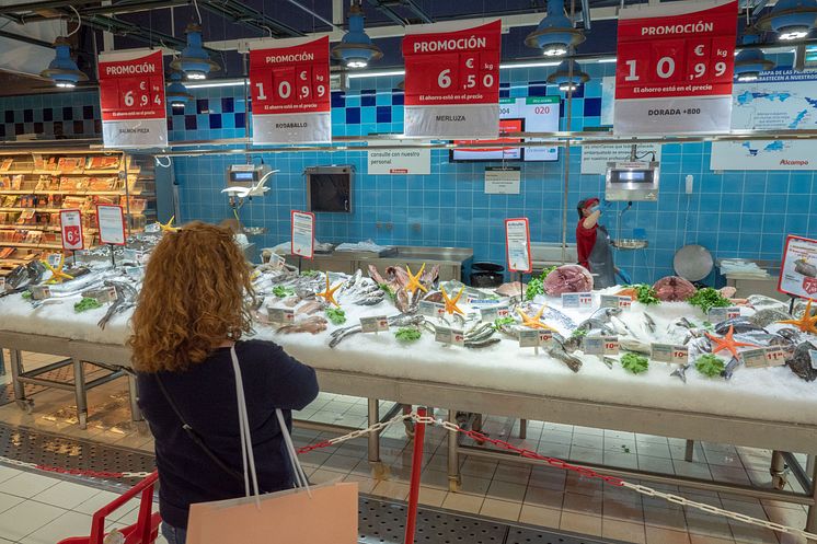 Bildet viser en dame som studerer utvalget av fisk og sjømat i en fersvaredisk i et supermarked i Spania