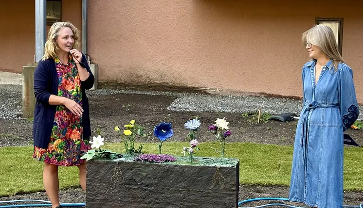 Konstnären Ebba Bohlin står på en gräsmatta intill verket Sju sorters blommor som är en bronsskulptur av växter. 