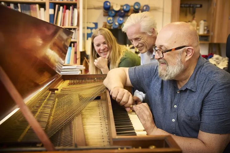 En kvinna och två män framför ett gammalt piano