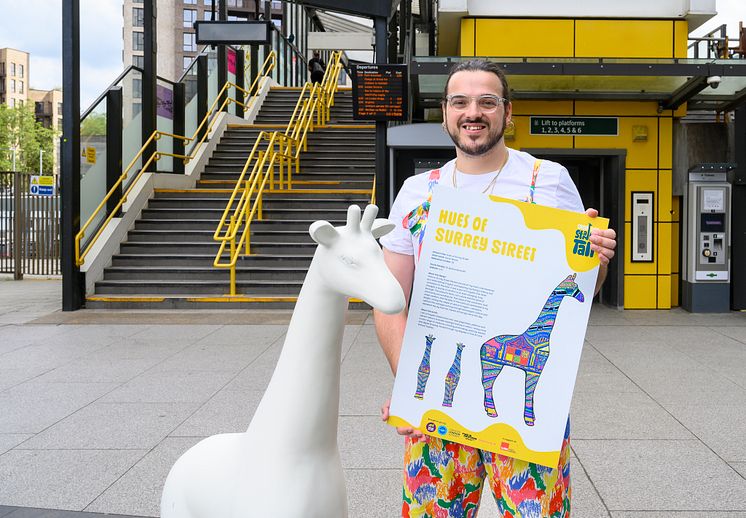 Artist, Aaron Bevan, poses outside of East Croydon station with one of the giraffe sculptures 