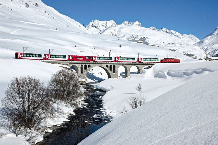 Der Glacier Express überquert im zugeschneiten Urserental in der Nähe des Dorfes Hospental im Kanton Uri die Furkareuss 