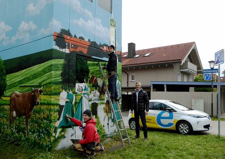 Heimatverbundenheit ziert Turmstation: Bayernwerk-Kommunalbetreuer Alexander Usselmann (rechts) besuchte die Art-EFX-Künstler Markus Ronge (links) und Pascal Sturm (Mitte) bei der Fertigstellung des Kunstwerks in Otterfing.