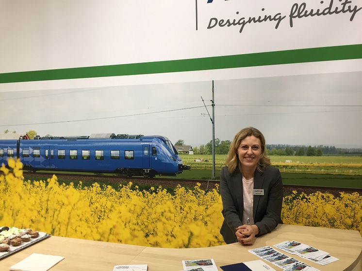 Maria Parent framför en bild på ett Pågatåg i Skåne. Ett exempel där Alstom har levererat regionaltåg till Sverige.