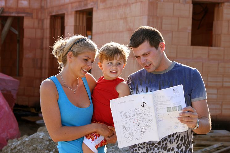 junge Familie vor Neubau im Sommer