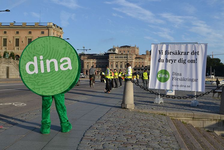 Maskot och tjänstemän från Dina Försäkringar delar ut reflexvästar till cyklister på Skeppsbron