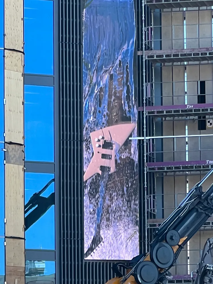 En elgitarr i ett vattenfall projiceras på en stor skärm på husets fasad.