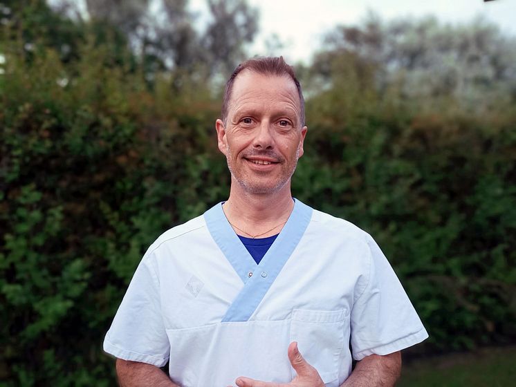 Porträtt av Magnus Ivarsson i arbetskläder, fotad mot en grön häck.