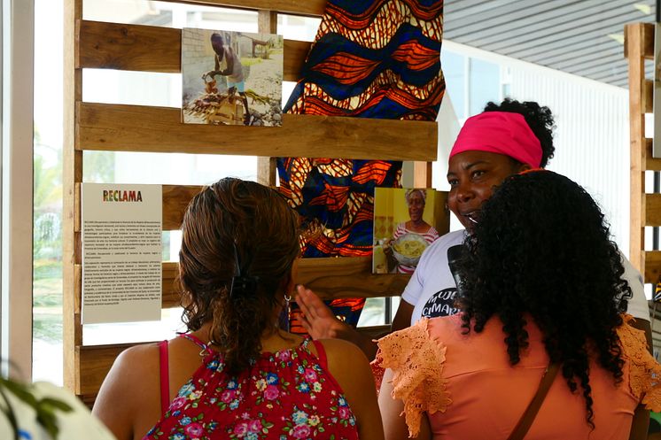 Peer researcher Evelia Quiñonez Bone takes visitors of the exhibition in Esmeraldas around some of the pictures created on the RECLAMA project, depicting gastronomy