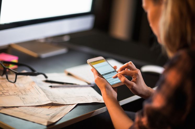 Businesswoman using smart phone-blue prints-Geber86_GettyImages