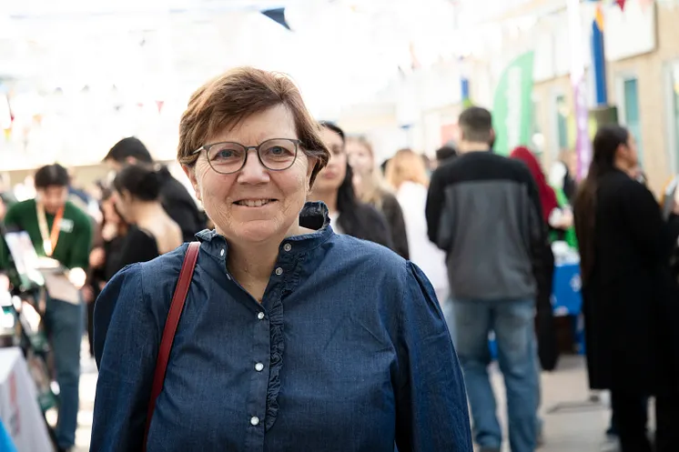 En kvinna med glasögon. Suddiga personer i bakgrunden. 