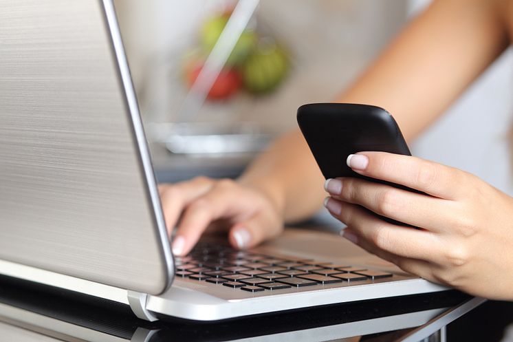 9994506-woman-hand-using-a-smart-phone-and-typing-a-laptop-at-home