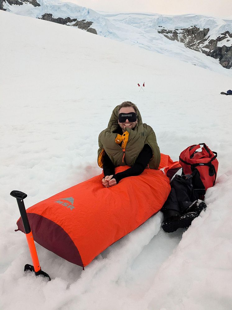 A man sits up in a bivvy bag, he's smiling with a   blackout eye mask for 24 hour daylight! 