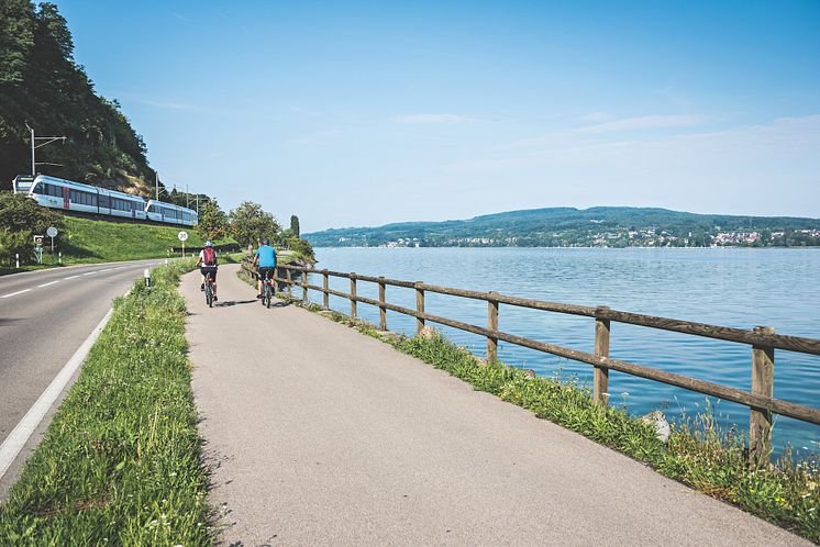 Tourenbiker Paar unterwegs am Bodensee bei Berlingen. Im Hintergrund der Thurbo Zug