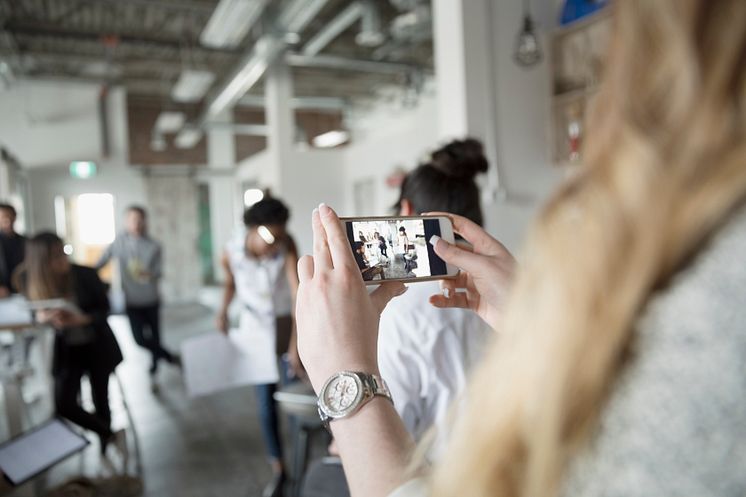 Creative businesswoman with camera phone videoing meeting in office