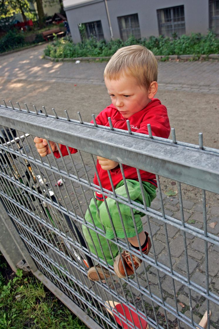 Junge klettert am Gitterzaun, Hochformat