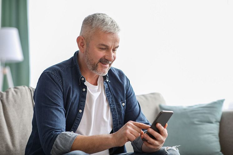 smiling senior man using smartphone while resting at home