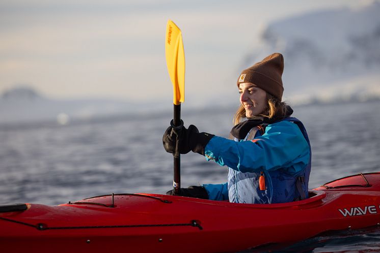 A solo women paddles in Antarctica's Orne Harbour in a hard shell kayak.