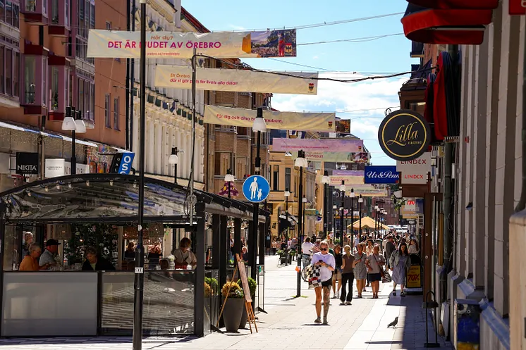 Köpmangatan med butiker, uteserveringar och besökare.